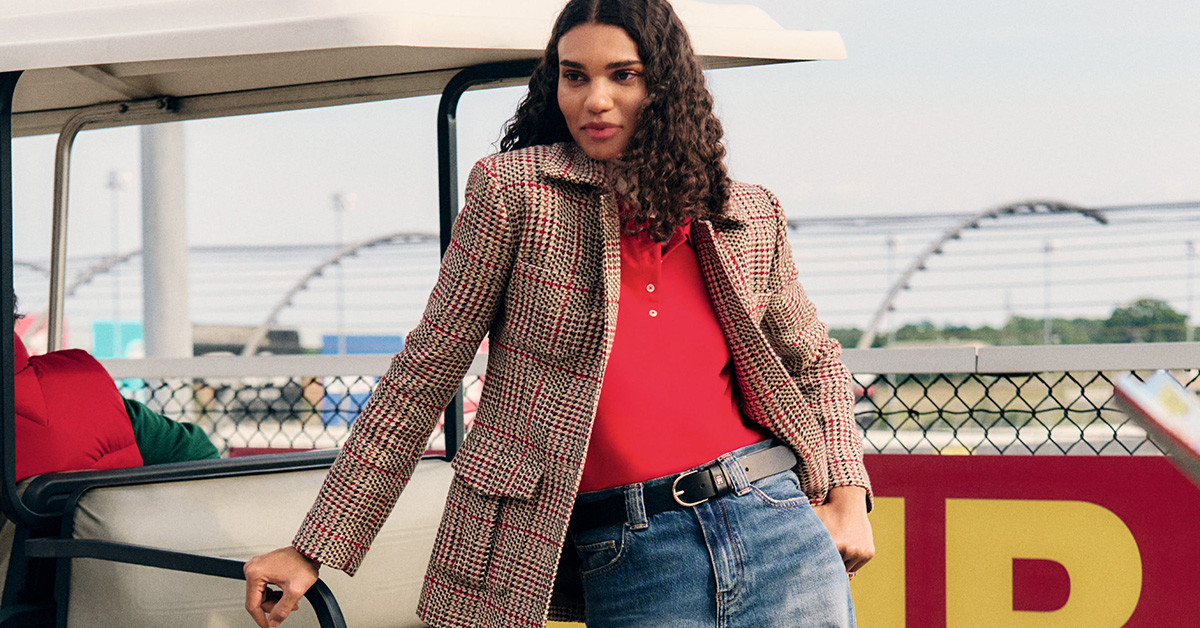 Kobieta w marynarce z kolorową kratą, czerwona koszulka polo, jeansy z czarnym paskiem, styl city casual na tle outdoorowym – modne stylizacje jesień/zima