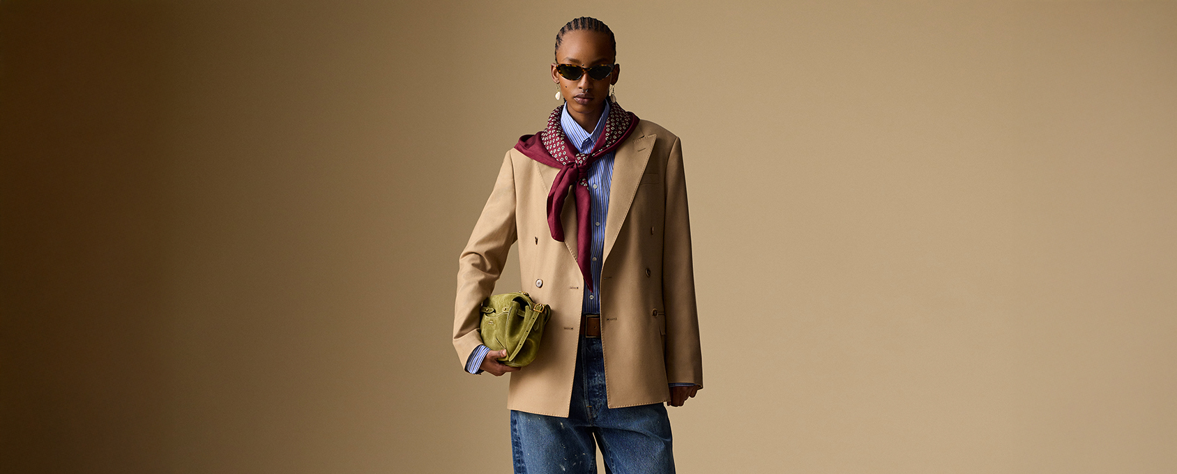 Mężczyzna w beżowej marynarce, niebieska koszula w paski, bordowa apaszka, szerokie jeansy, oliwkowo-zielona torba, stylizacja smart casual na jesień/zima