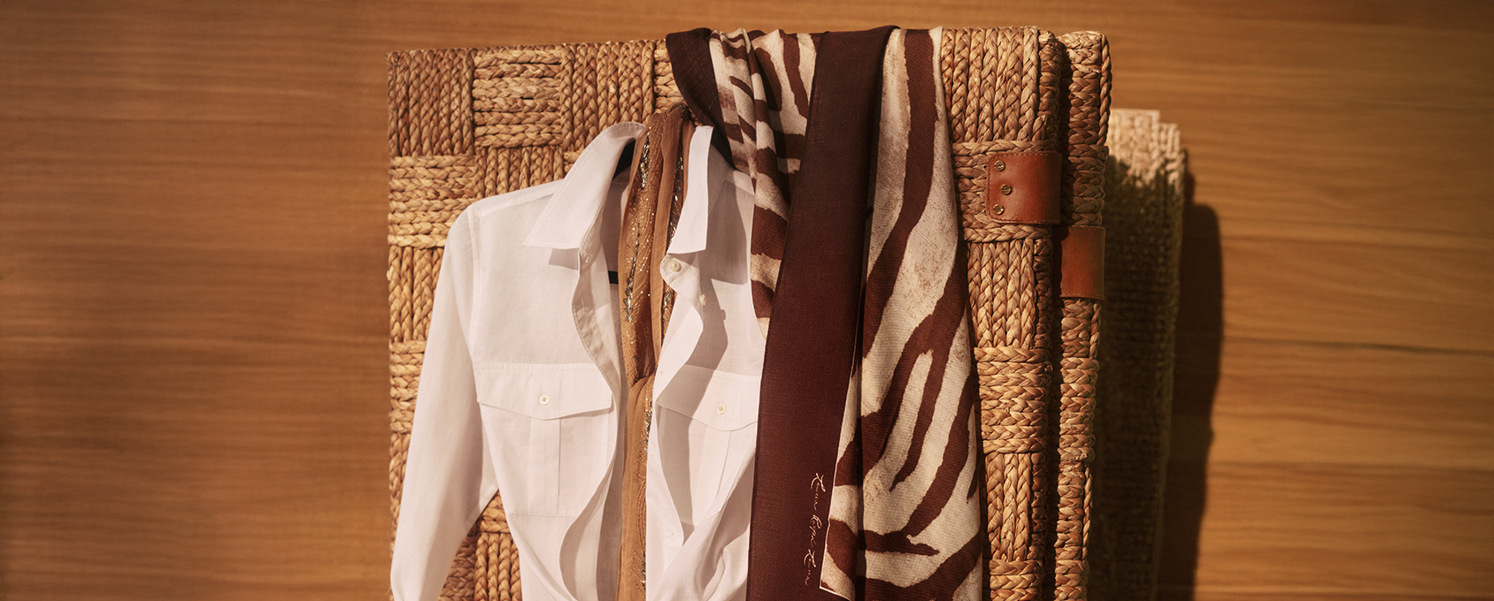 Biała koszula z kołnierzykiem zawieszona na plecionym koszu, brązowy szalik w zwierzęcy wzór zebra, beżowy szalik – inspiracja modą safari, stylizacje dodatków na sezon jesień/zima