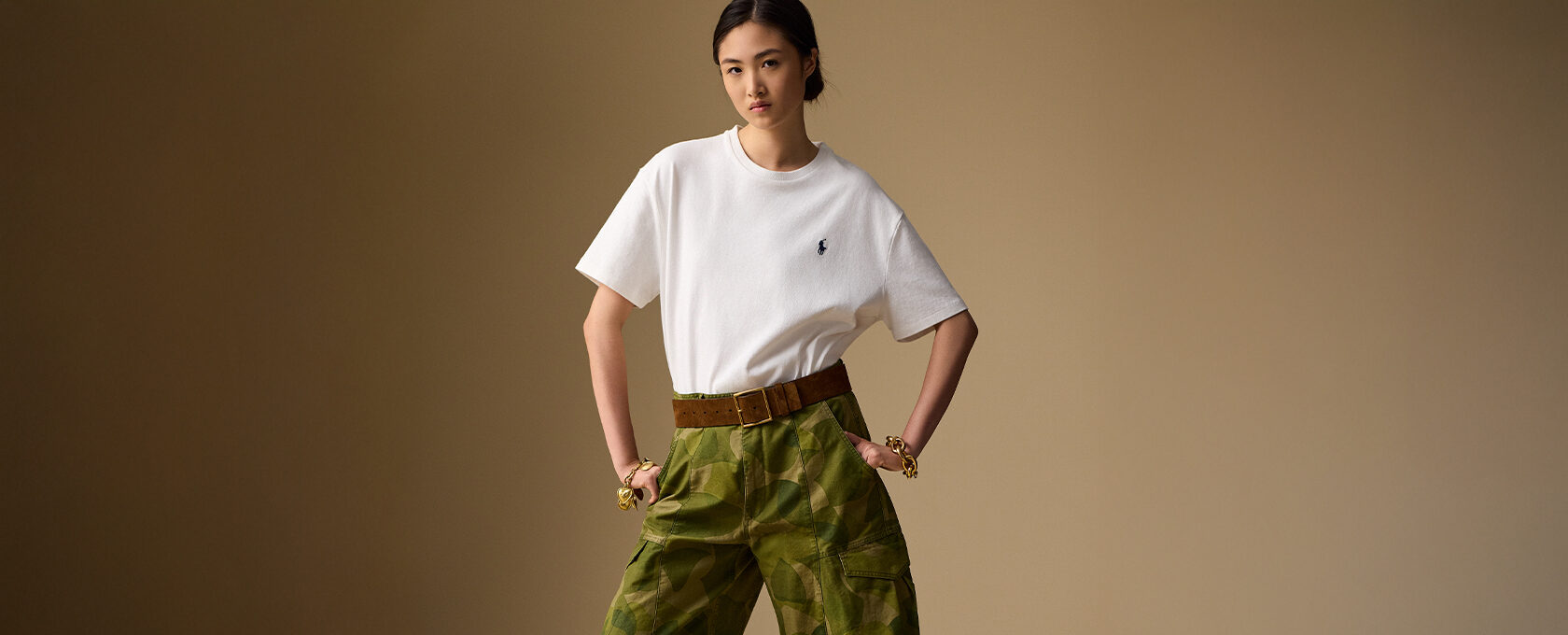 Kobieta w białym t-shircie z logo i szerokich zielonych spodniach cargo w kamuflaż, brązowy pasek, minimalistyczny look w stylu militarnym – moda streetwear damska jesień/zima